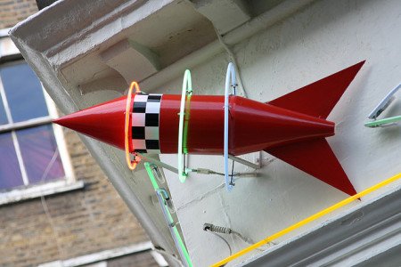 A red stylized rocket with neon rings around it