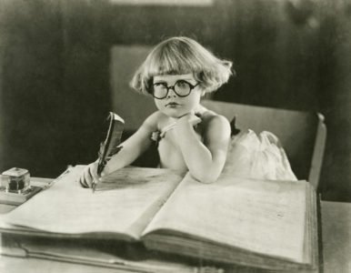 A young girl wearing round glasses and writing in a large ledger with a quill pen