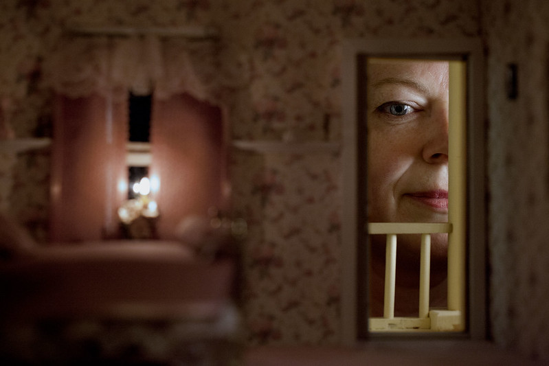 Image: inside of a dollhouse, with a woman looking in through the window