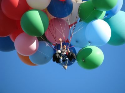 Image: man in the air, held aloft by dozens of balloons