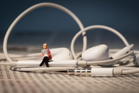 Image: miniature figure sitting atop a pair of wired earbuds, reading aloud