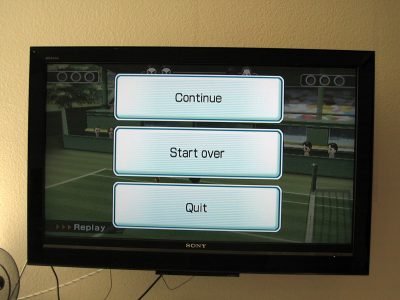 Image: television displaying a video game menu of three buttons labeled Continue, Start Over, and Quit