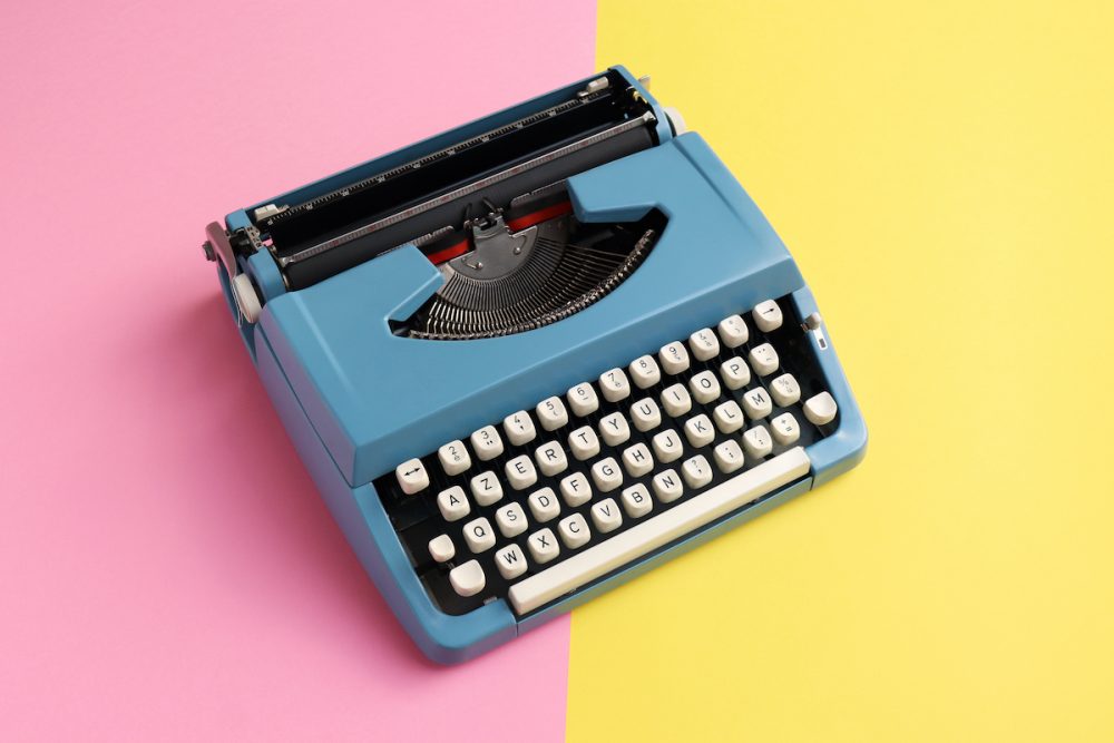 Image: vintage blue typewriter on a background that's half pink and half yellow