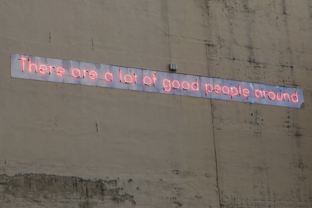 Image: art installation on the side of a building, made of neon letters spelling the sentence "There are a lot of good people around."