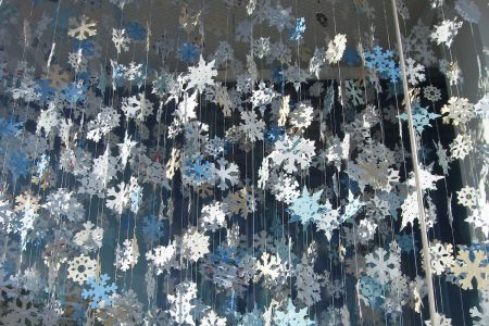 Image: hundreds of paper snowflakes hanging by threads from a ceiling