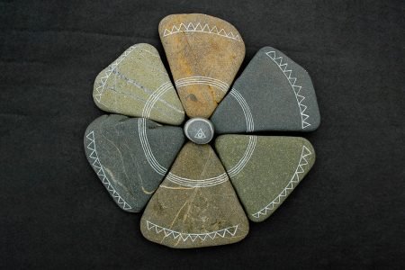 Image: six flat triangular stones arranged in a circle, with a small round stone at their center