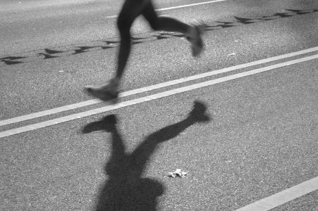 Image: legs and shadow of a lone runner in the middle of a city street
