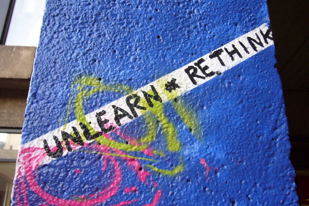 Image: urban wall with graffiti reading "Unlearn and rethink."