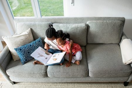 Image: two young Black girls sitting together on a couch, reading a picture book.