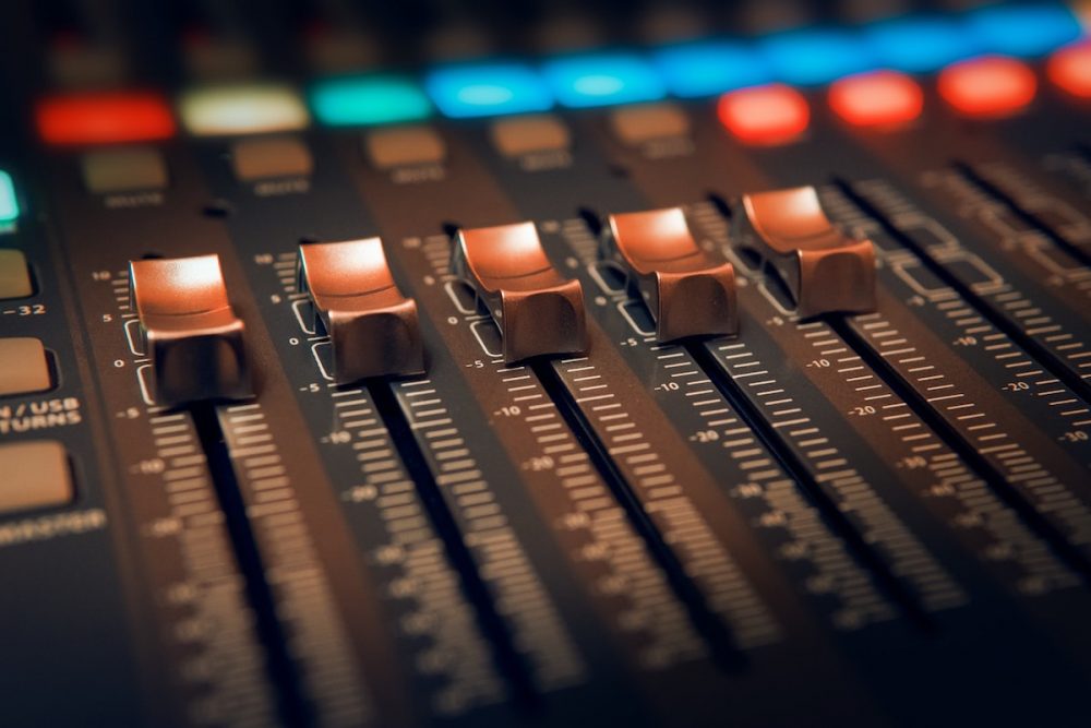 Image: faders on an audio mixing console.