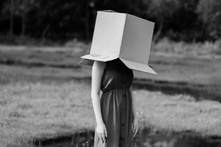 Image: woman standing in a field, with a large box over her head.