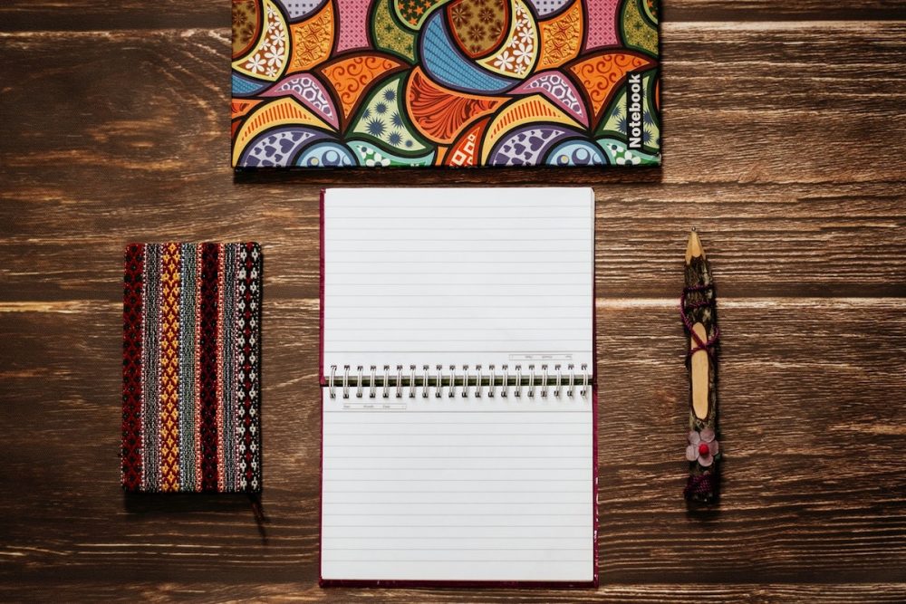 Image: a colorful notebook, pencil case, pencil and open day planner on a wooden table.