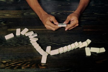 Image: Hands holding a domino, over a stack of fallen dominoes.