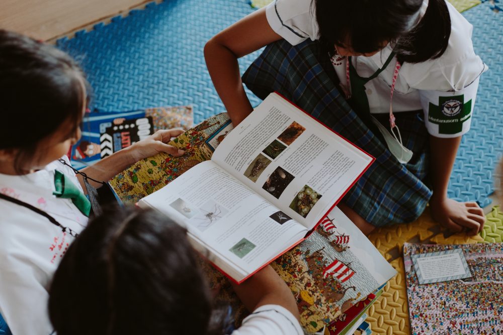 Image: three schoolgirls gathered around a stack of picture books.