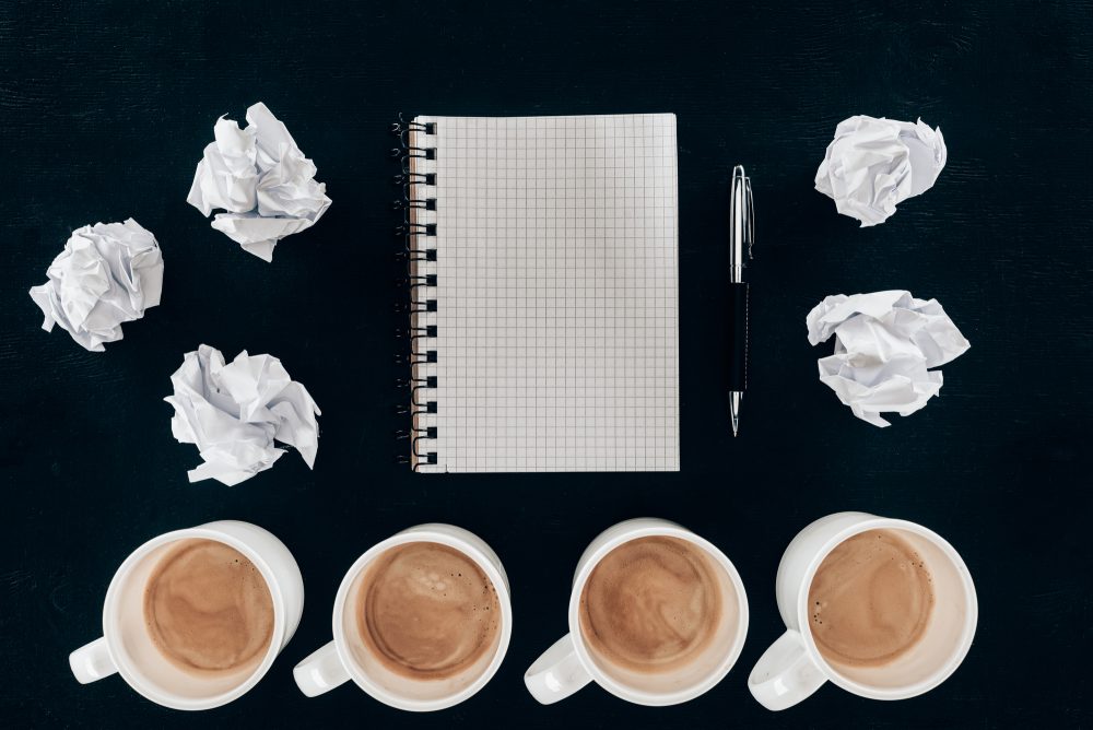 Image: Grid notebook surrounded by crumpled balls of paper and half-full coffee mugs.