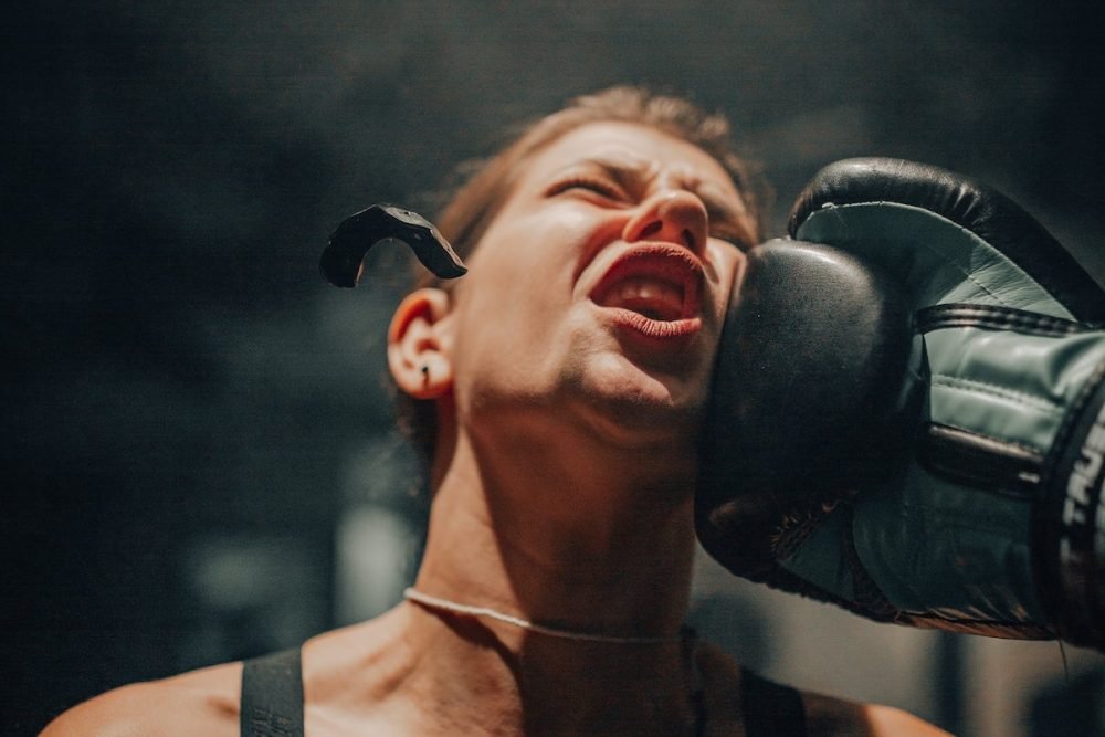 Image: a female boxer being punched, sending her protective mouthguard flying into the air.