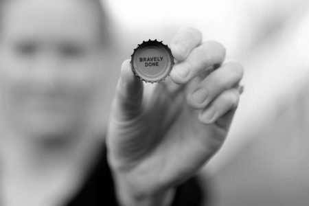 Image: Hand holding a bottle cap with "Bravely done" printed on the inside.