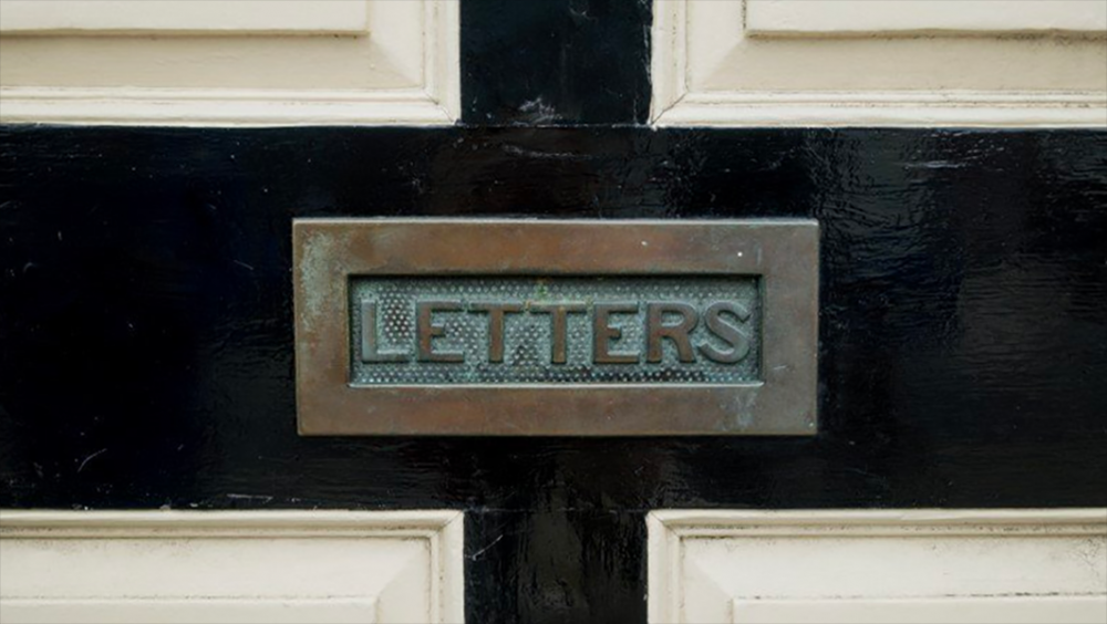 Image: patinaed brass slot labeled "Letters" set into an exterior door.