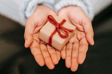 Image: a woman's open hands holding a small, wrapped gift.