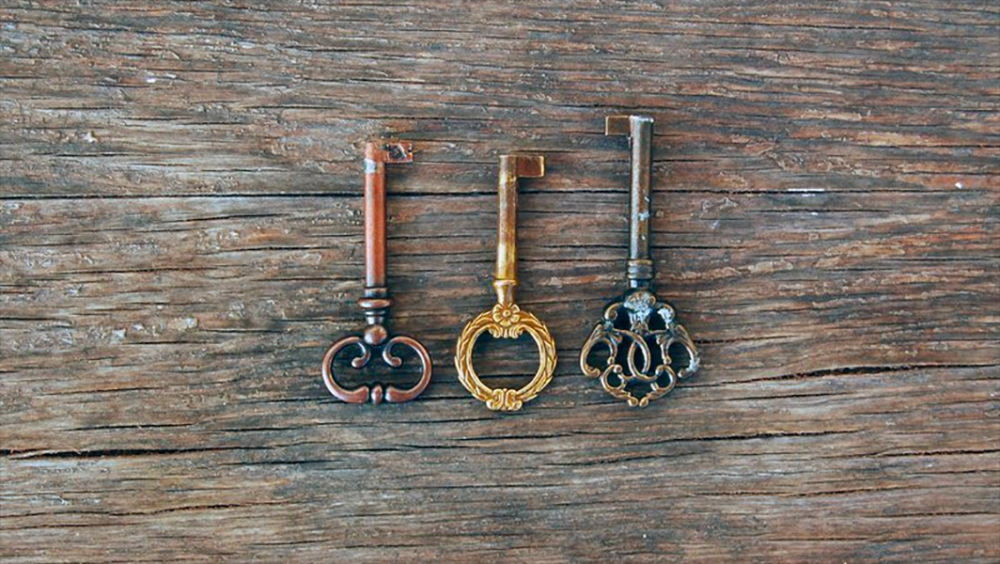 Image: three decorative antique keys arranged on a rough wooden surface.