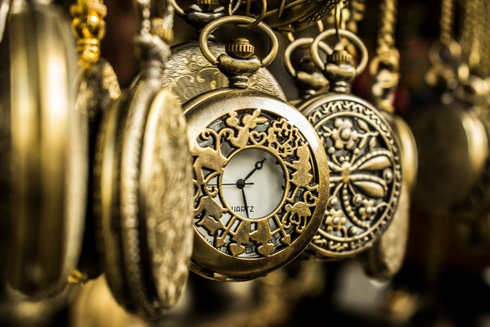 Image: numerous antique brass pocket watches hanging in a row.
