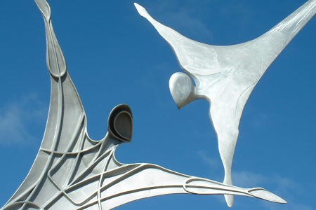 Image: outdoor sculpture of two figures, one showing a smooth exterior and the other showing internal structures.