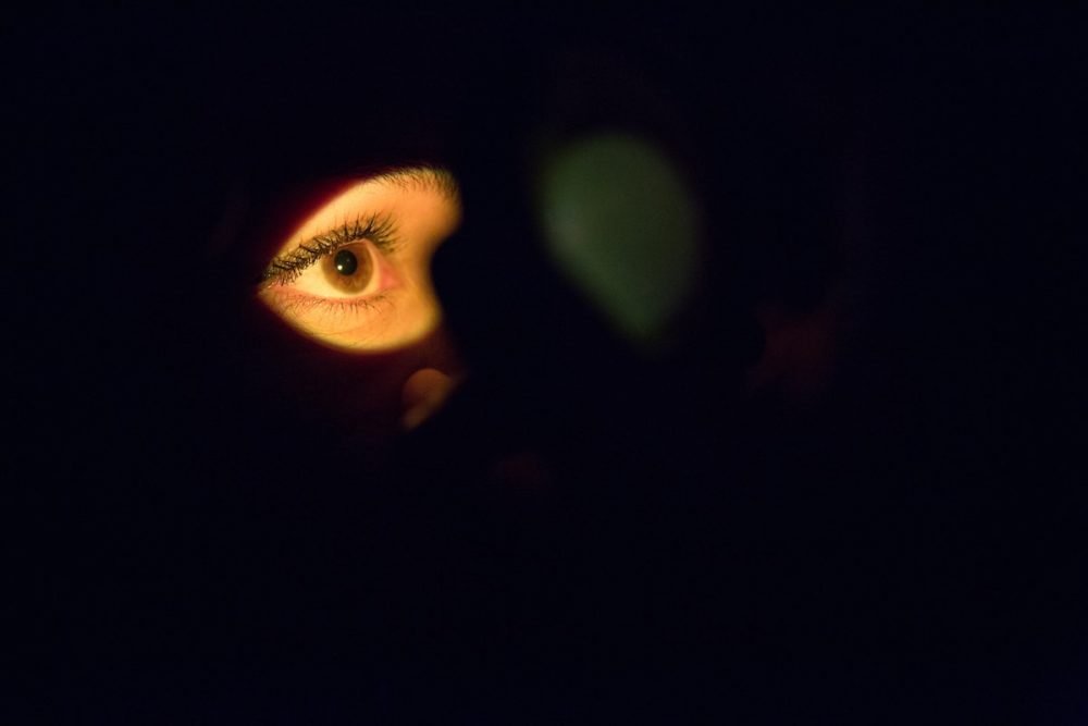 Image: in a darkened space, a light illuminates a woman's eye gazing intently.