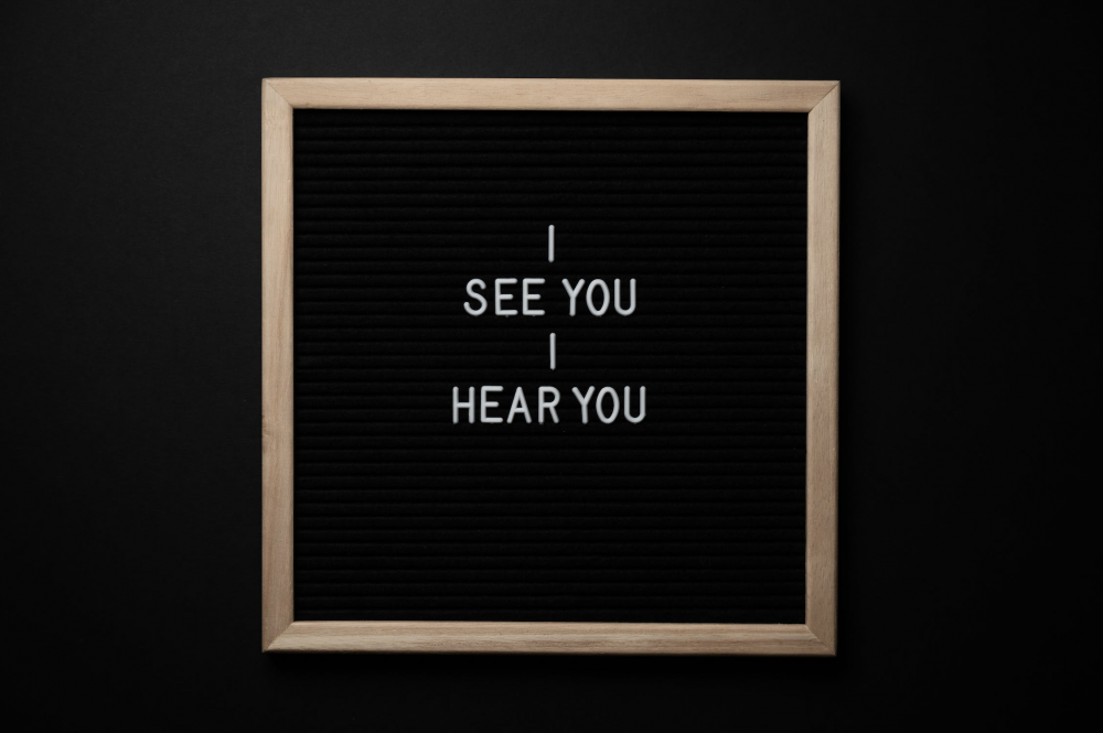 a small sign with a wooden frame, around the words "I see you, I hear you" on a black background