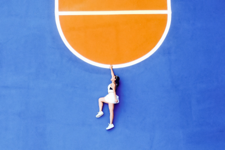 Image: aerial view of woman in sportswear lying on a gymnasium floor. From this angle, she appears to be hanging from a semi-circular line painted on the floor.