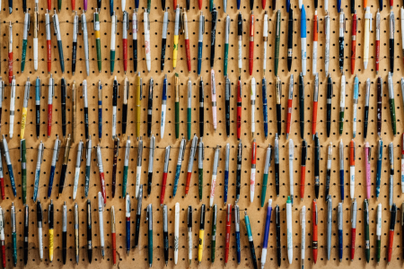 Image: pegboard on a wall, with hundreds of different ballpoint pens hooked to the surface.