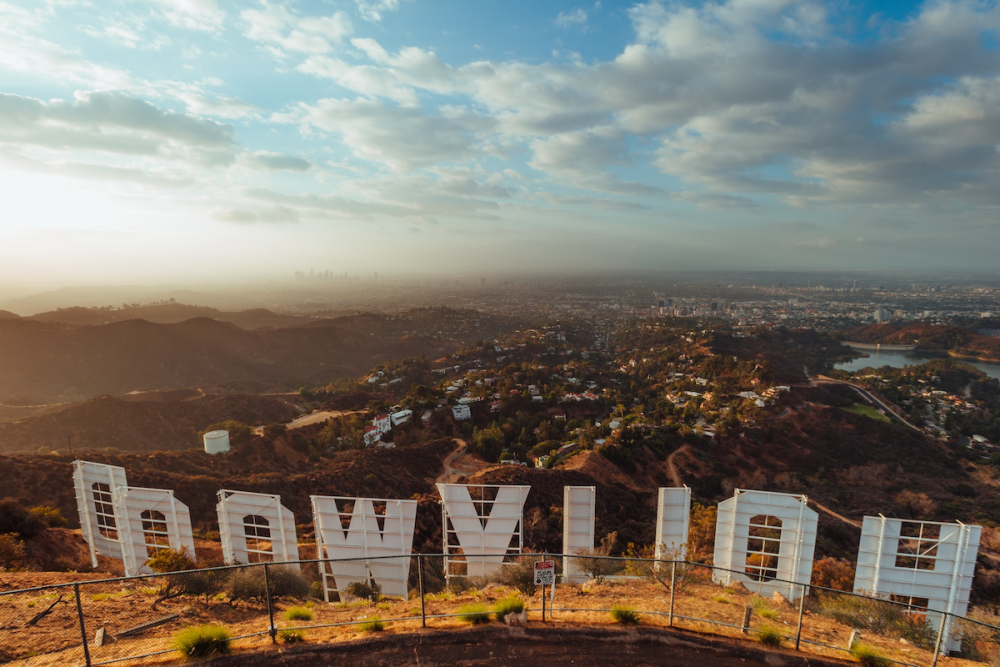 Image: behind a fence, the back of the Hollywood Sign looms over the valley below.