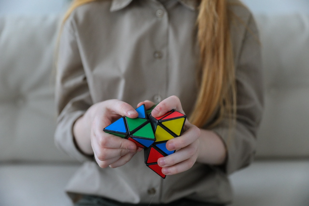 Image: the hands of a young woman solving a Pyraminx, a pyramid-shaped Rubik's Cube-style puzzle.