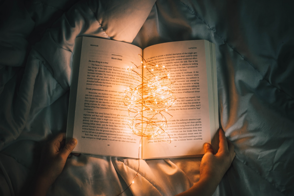 Image: someone hold a book open on bedclothes in a darkened room. On the open pages of the book is a jumble of tiny illuminated L.E.D. lights.