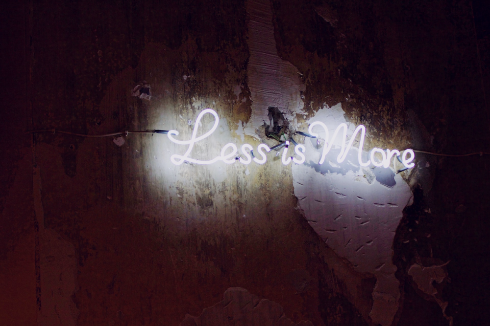 Image: a neon sign reading "Less Is More" is mounted on a roughly-finished wall.
