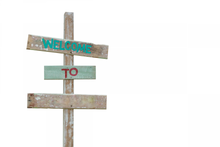 Image: an antique wooden signpost on a white background. Painted on the sign is "Welcome to [blank]".