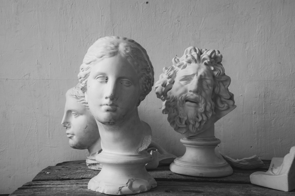 Image: three antique sculpted heads on pedestals sit on a rough wooden table.
