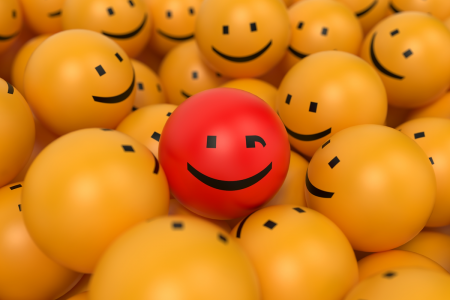 Image: at the center of a pile of yellow smiley-faced orbs is a red one with a winking face.