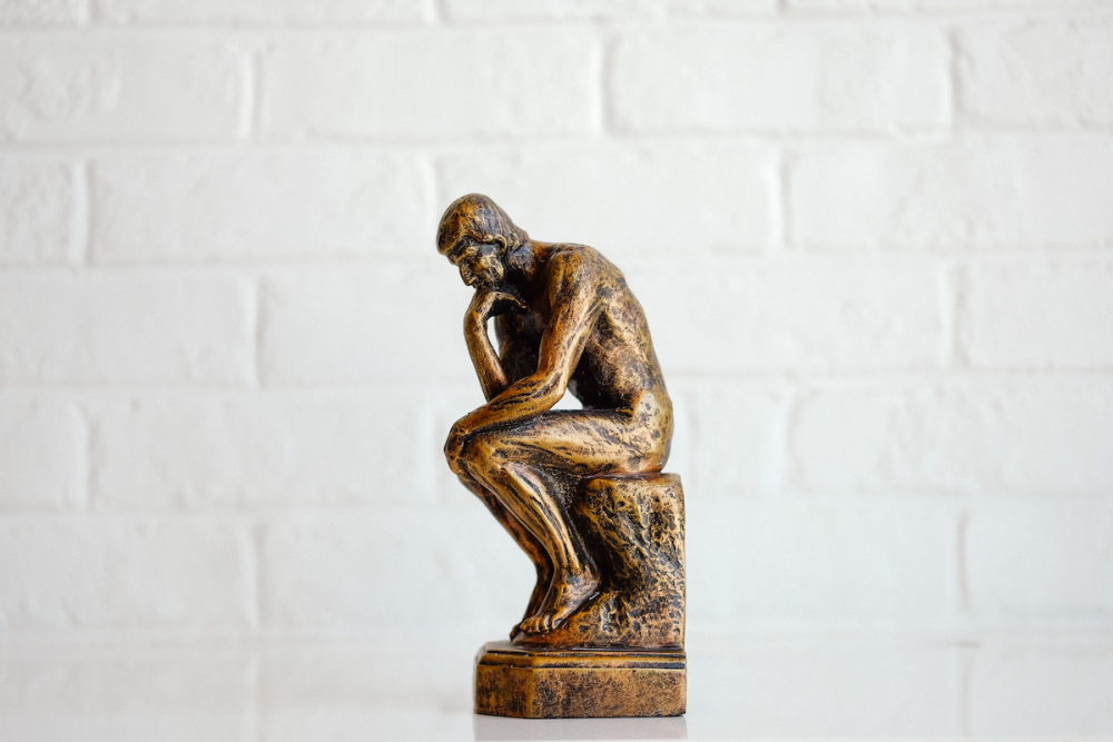 Image: a miniature of Rodin's The Thinker, painted gold, sits against a white background.