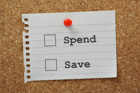 Image: tacked to a cork bulletin board is a scrap of paper on which are two choices written, "Spend" and "Save", with empty check-boxes beside them.