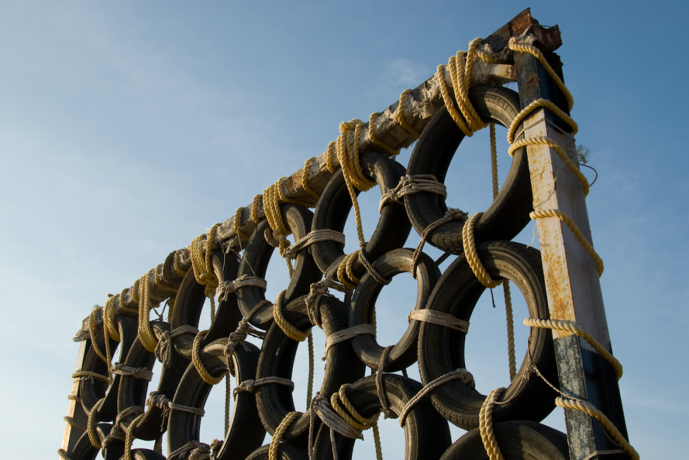 Image: as part of an obstacle course, automobile tires are tied together with rope and mounted in a tall metal frame that looms against a blue sky.