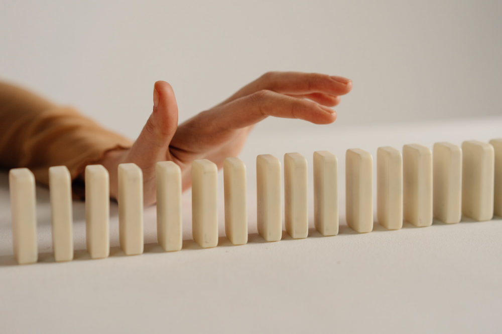 Image: a woman's hand hovers above a row of standing dominoes.