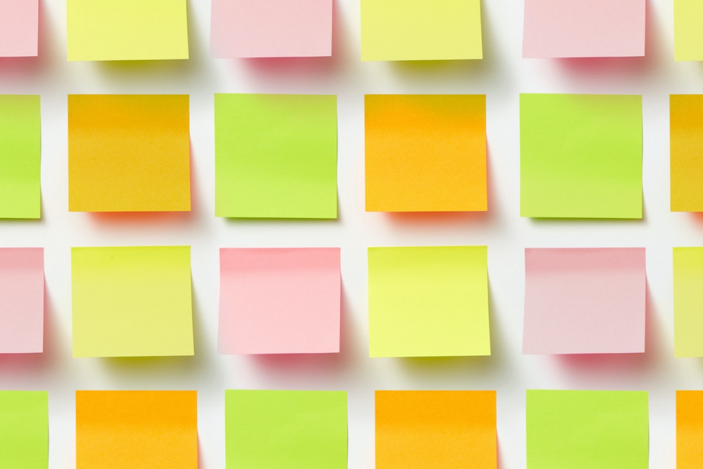Image: Pink, orange, green and yellow sticky-notes are arranged in a grid on a white wall.