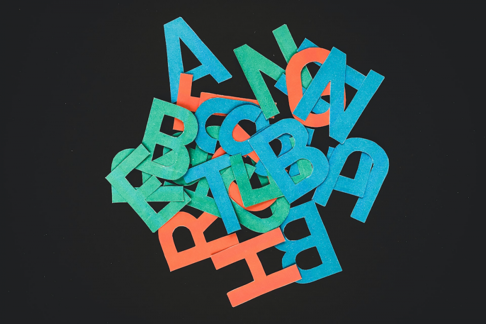 Image: alphabet letters cut from various colors of craft paper are jumbled on a black background.