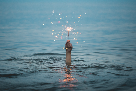 From underwater a lone hand emerges, holding a sparkler.