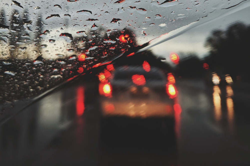 Image: the view of cars on a UK motorway as seen through a rainy windscreen at dawn.