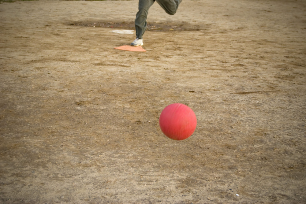 Image: on a playing field, a red kickball hurls toward someone who's poised to kick it.
